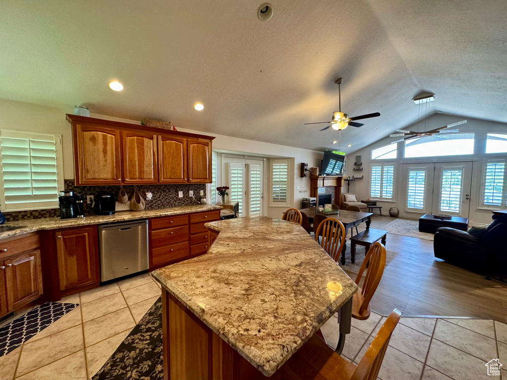 Kitchen with stainless steel dishwasher, a ceiling fan, open floor plan, vaulted ceiling, and backsplash