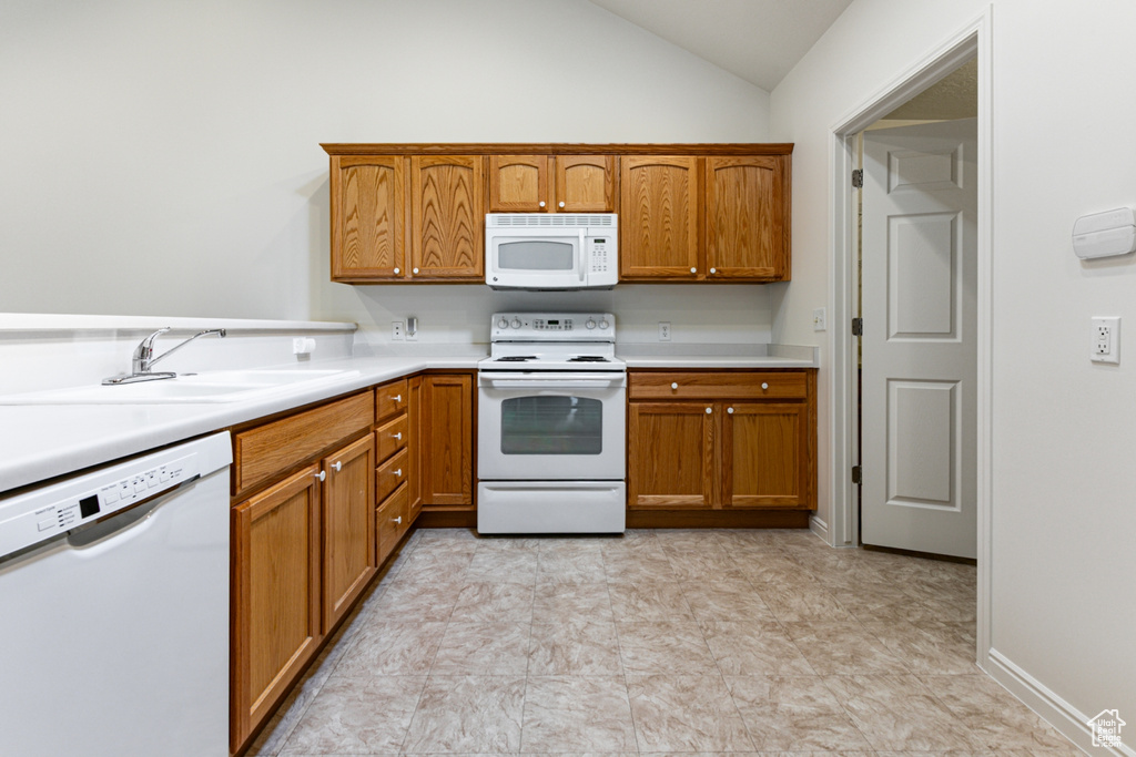 Kitchen featuring white appliances, a sink, light countertops, vaulted ceiling, and brown cabinets
