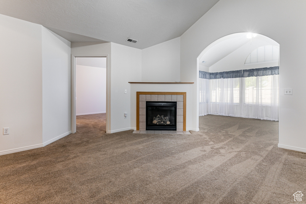 Unfurnished living room featuring carpet flooring, lofted ceiling, a tiled fireplace, and baseboards