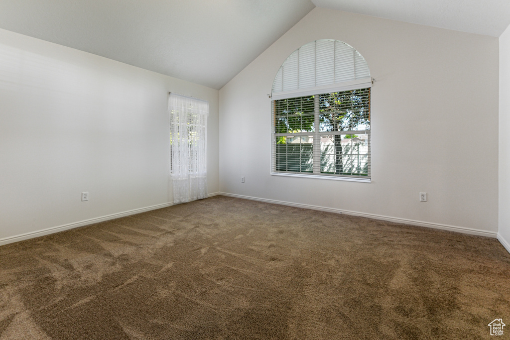 Carpeted spare room featuring vaulted ceiling and baseboards