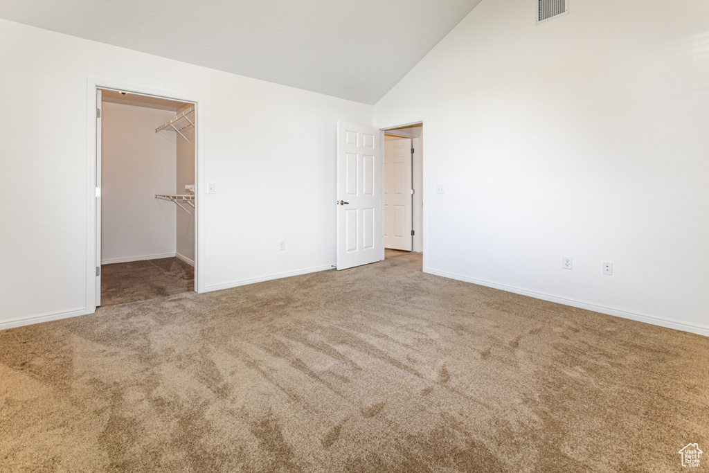 Unfurnished bedroom with carpet floors, a spacious closet, baseboards, and high vaulted ceiling