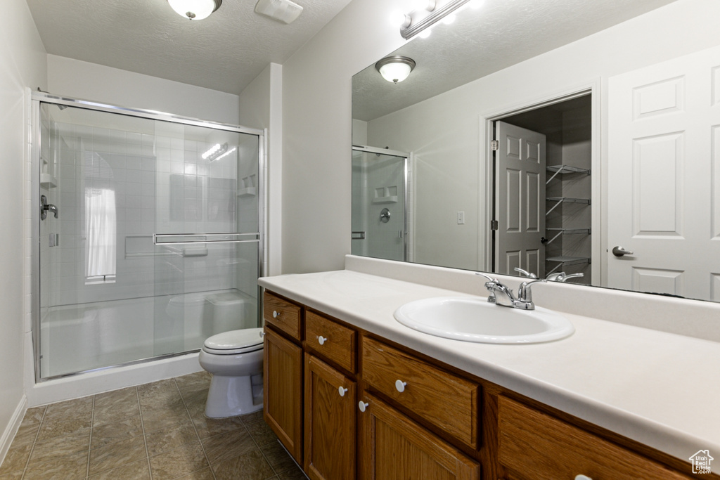 Full bath with a stall shower, vanity, toilet, baseboards, and a textured ceiling