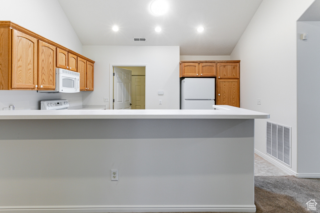 Kitchen with white appliances, lofted ceiling, a peninsula, dark colored carpet, and light countertops