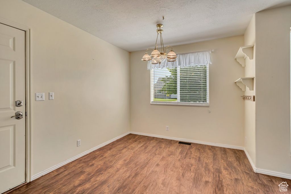 Spare room with a chandelier, wood finished floors, baseboards, and a textured ceiling
