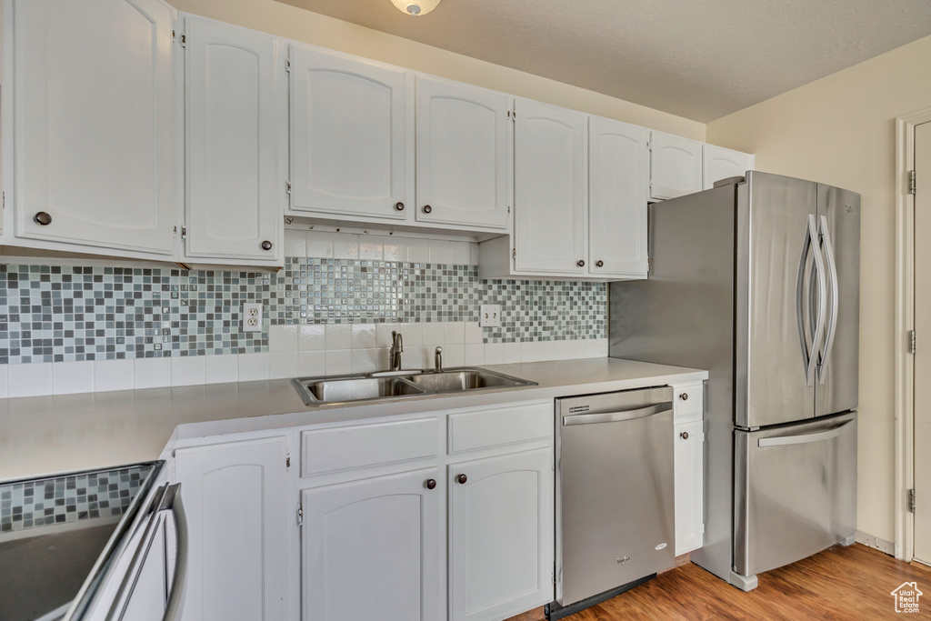 Kitchen featuring stainless steel appliances, a sink, tasteful backsplash, light wood-type flooring, and light countertops