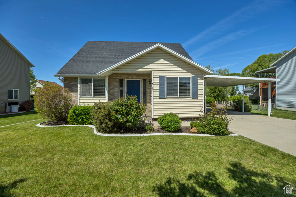 View of front facade with concrete driveway, an attached carport, a front lawn, and roof with shingles