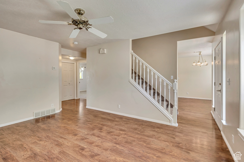 Spare room with wood finished floors, stairs, a ceiling fan, and a chandelier
