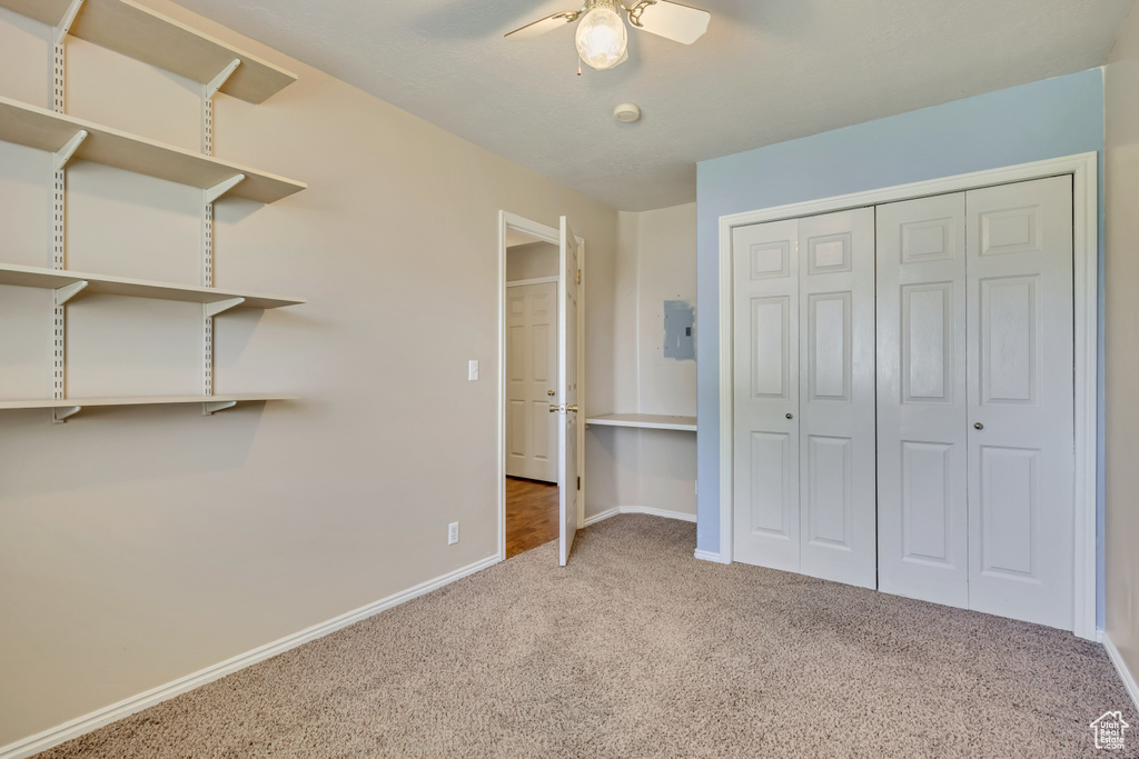 Unfurnished bedroom with carpet, electric panel, baseboards, a closet, and ceiling fan