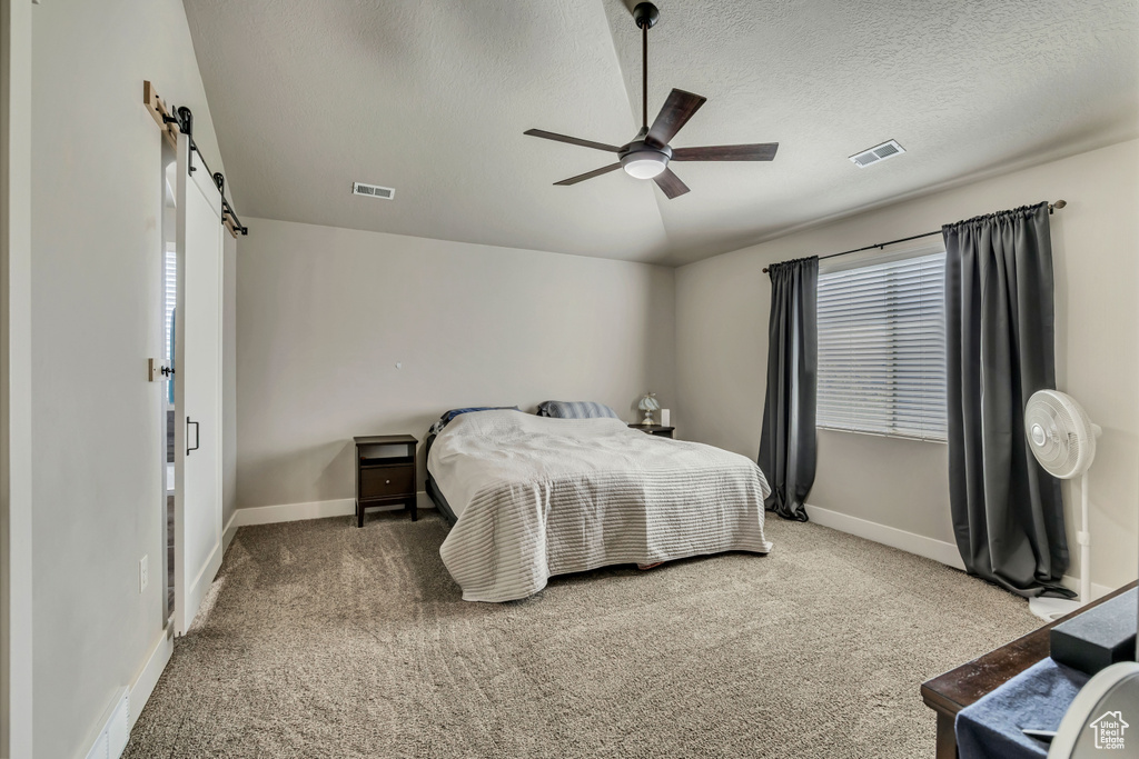 Bedroom with a barn door, carpet, baseboards, and a textured ceiling