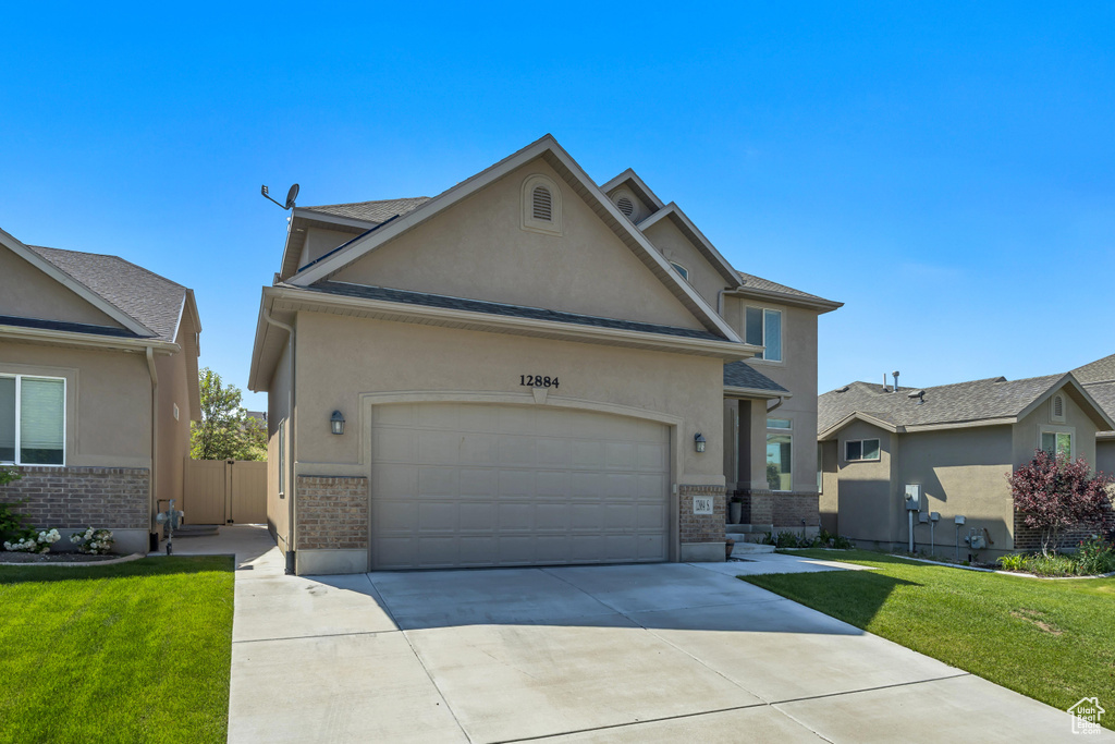 Traditional home with brick siding, stucco siding, driveway, and a front yard