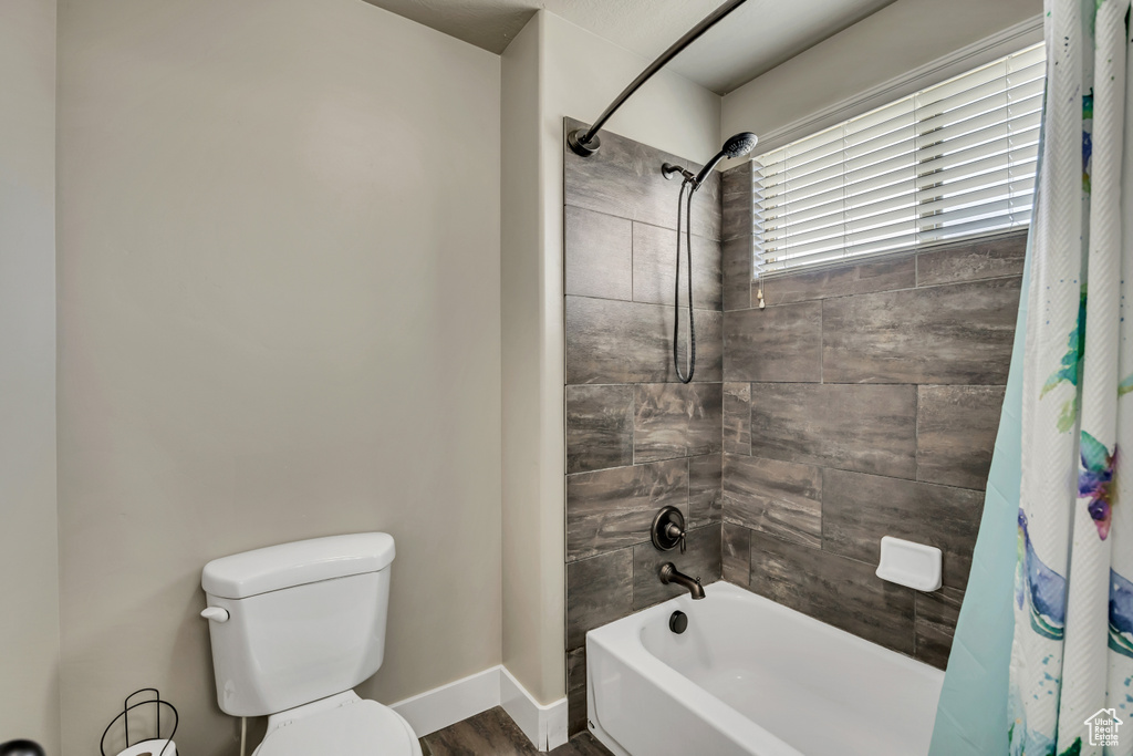 Bathroom with shower / bath combo, toilet, wood finished floors, and baseboards