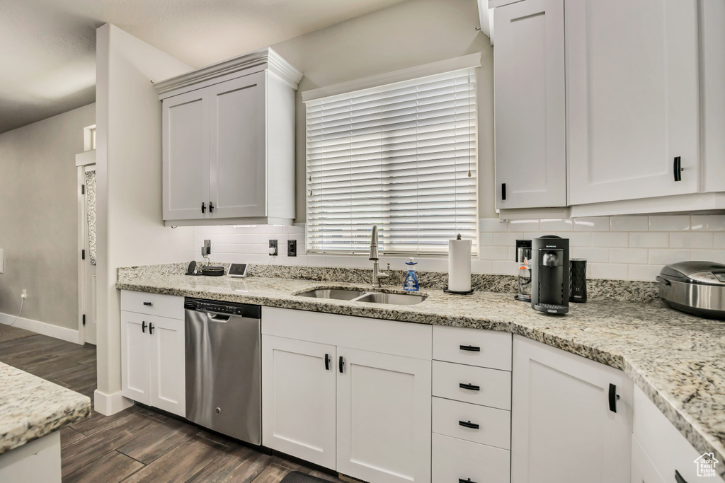 Kitchen featuring stainless steel dishwasher, a sink, dark wood-type flooring, backsplash, and white cabinets