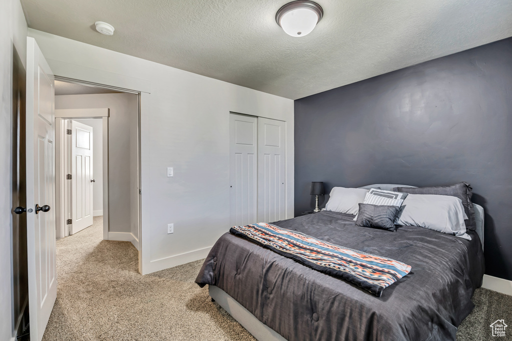 Bedroom featuring light colored carpet, a textured ceiling, a closet, and baseboards