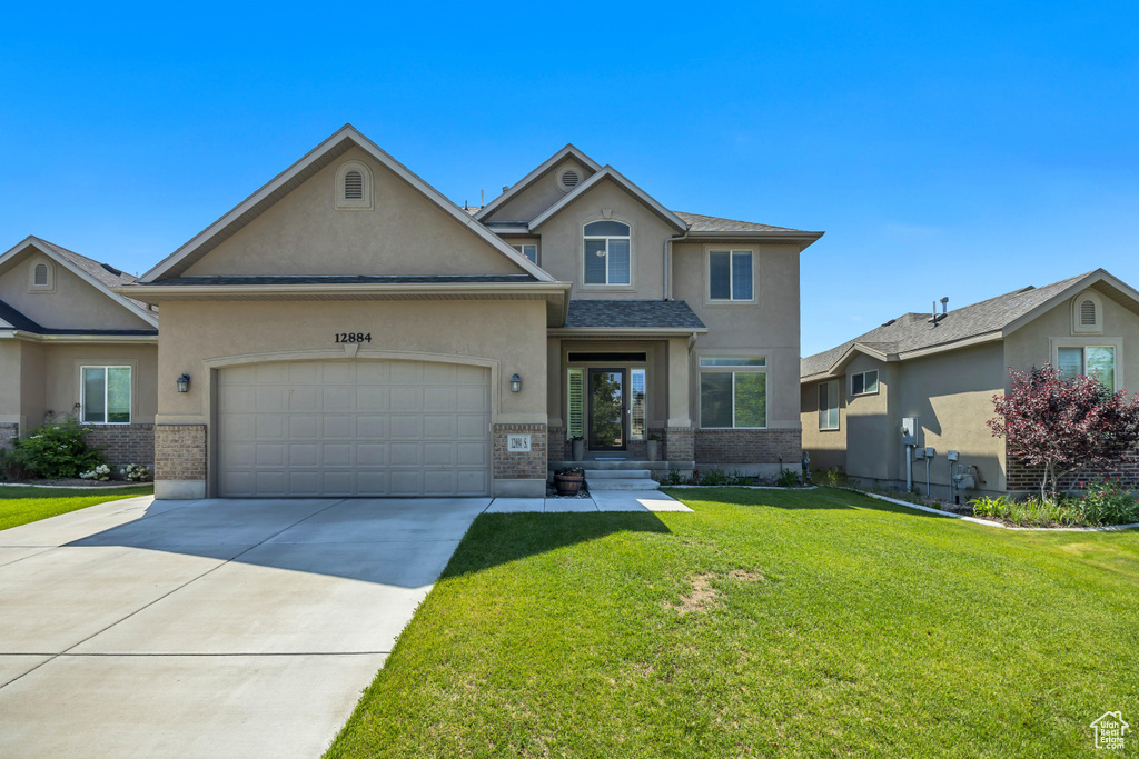 Traditional home with stucco siding, a garage, concrete driveway, brick siding, and a front yard