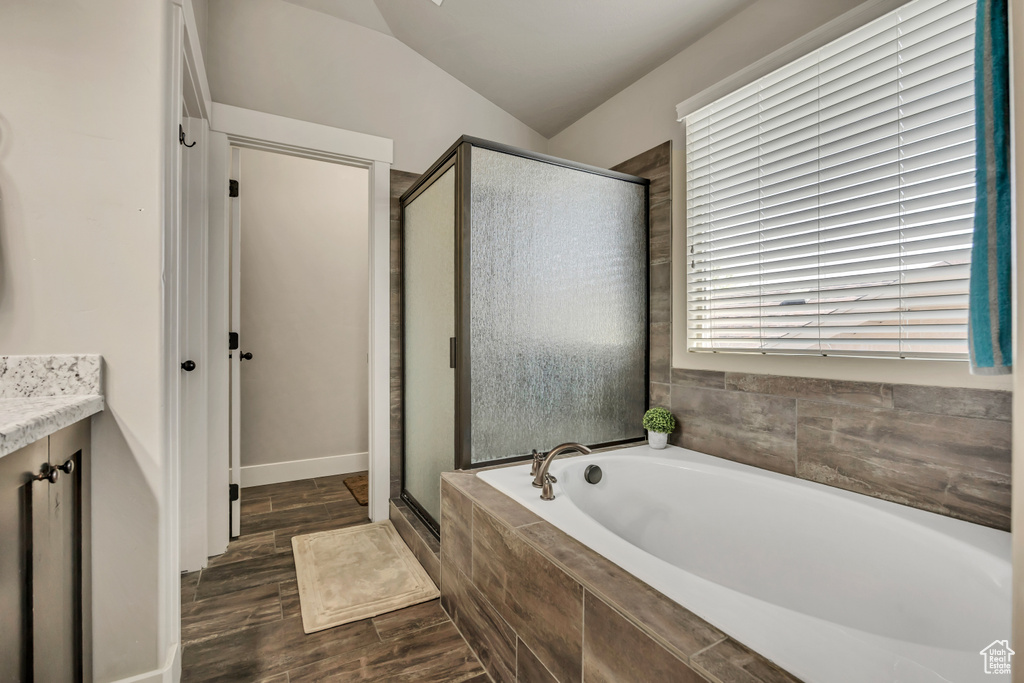 Full bath with a bath, a shower stall, vanity, wood finished floors, and lofted ceiling
