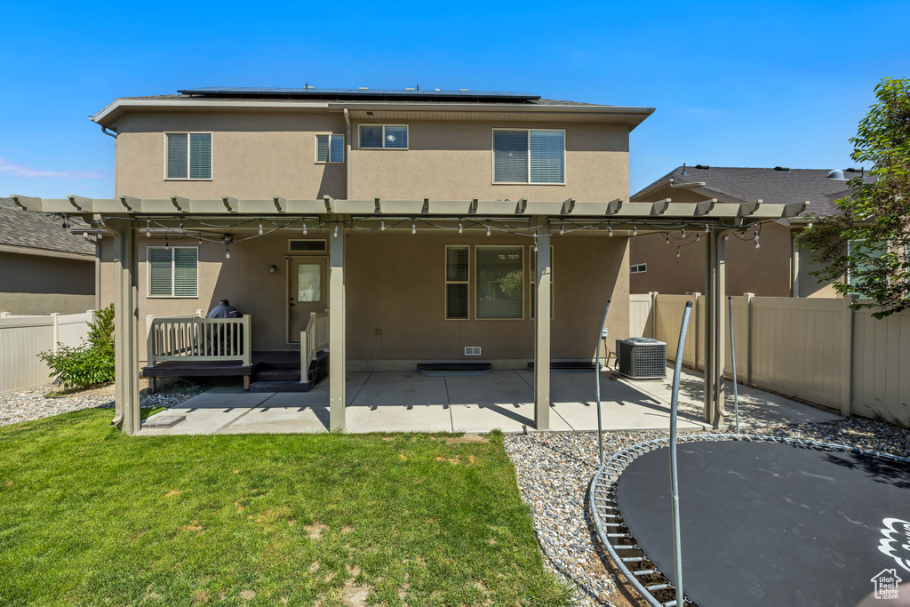 Rear view of house with stucco siding, a pergola, central AC unit, and solar panels