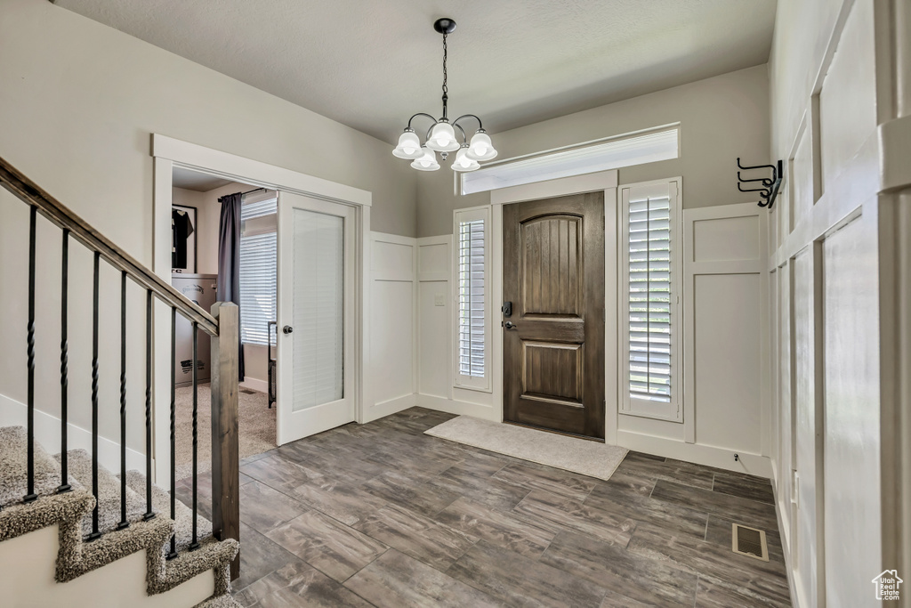Entrance foyer with stairs, a decorative wall, dark wood-style floors, and a chandelier