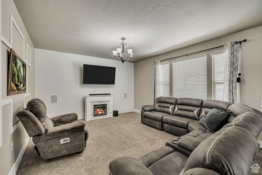 Living area with carpet flooring, a chandelier, a warm lit fireplace, a textured ceiling, and baseboards