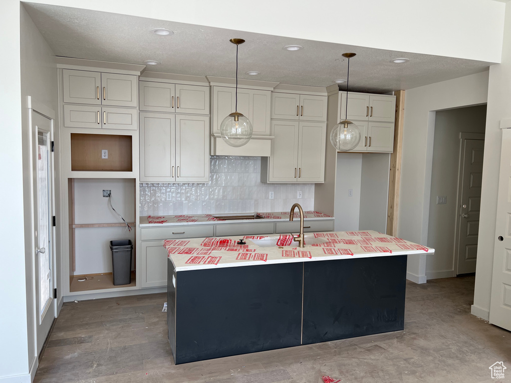 Kitchen featuring an island with sink, decorative backsplash, light countertops, recessed lighting, and hanging light fixtures