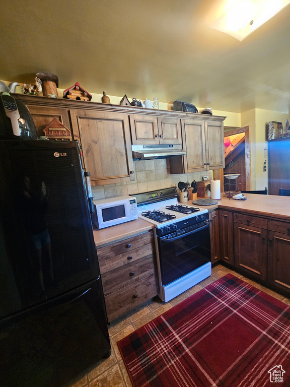 Kitchen featuring freestanding refrigerator, white microwave, range with gas stovetop, under cabinet range hood, and light countertops