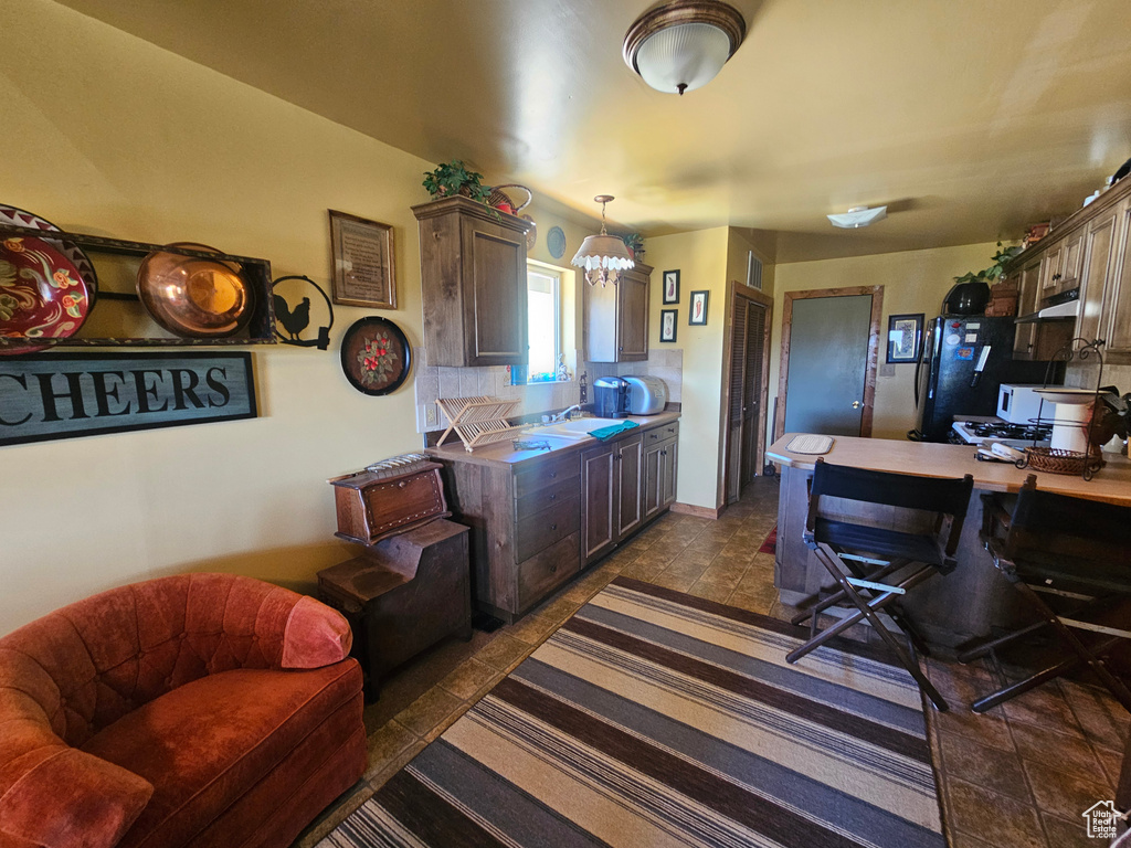 Kitchen featuring under cabinet range hood, freestanding refrigerator, a chandelier, backsplash, and a sink