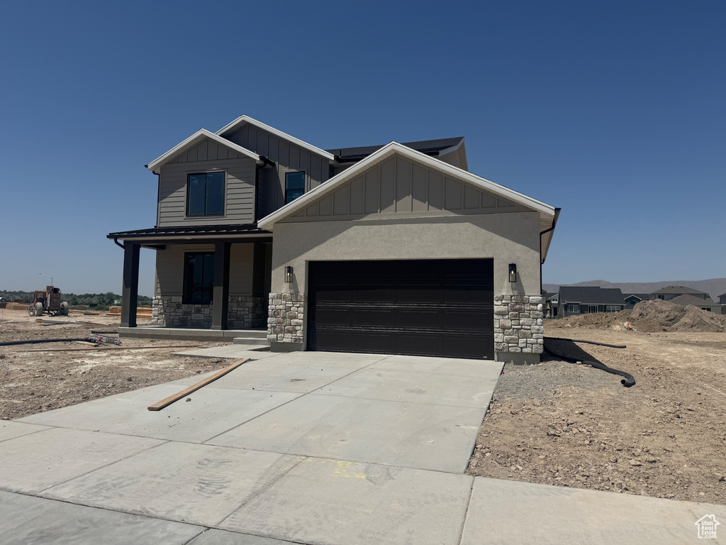 View of front of house featuring stone siding, a garage, solar panels, board and batten siding, and driveway