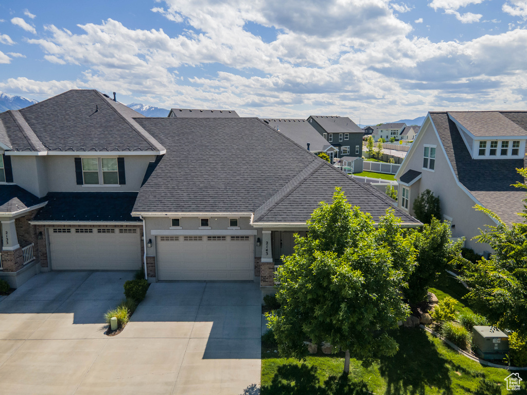 View of front facade featuring a residential view, stucco siding, driveway, roof with shingles, and an attached garage