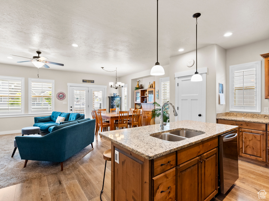 Kitchen featuring a sink, brown cabinets, dishwasher, a center island with sink, and recessed lighting