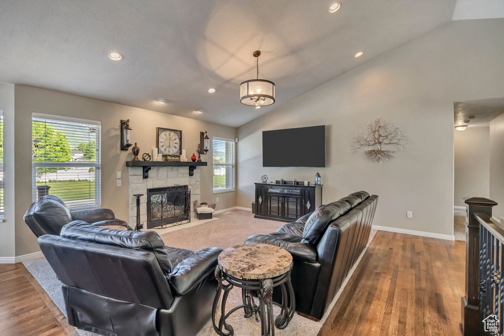 Living room featuring a stone fireplace, vaulted ceiling, baseboards, recessed lighting, and wood finished floors