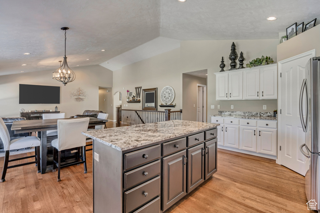 Kitchen featuring freestanding refrigerator, vaulted ceiling, white cabinets, open floor plan, and a kitchen island