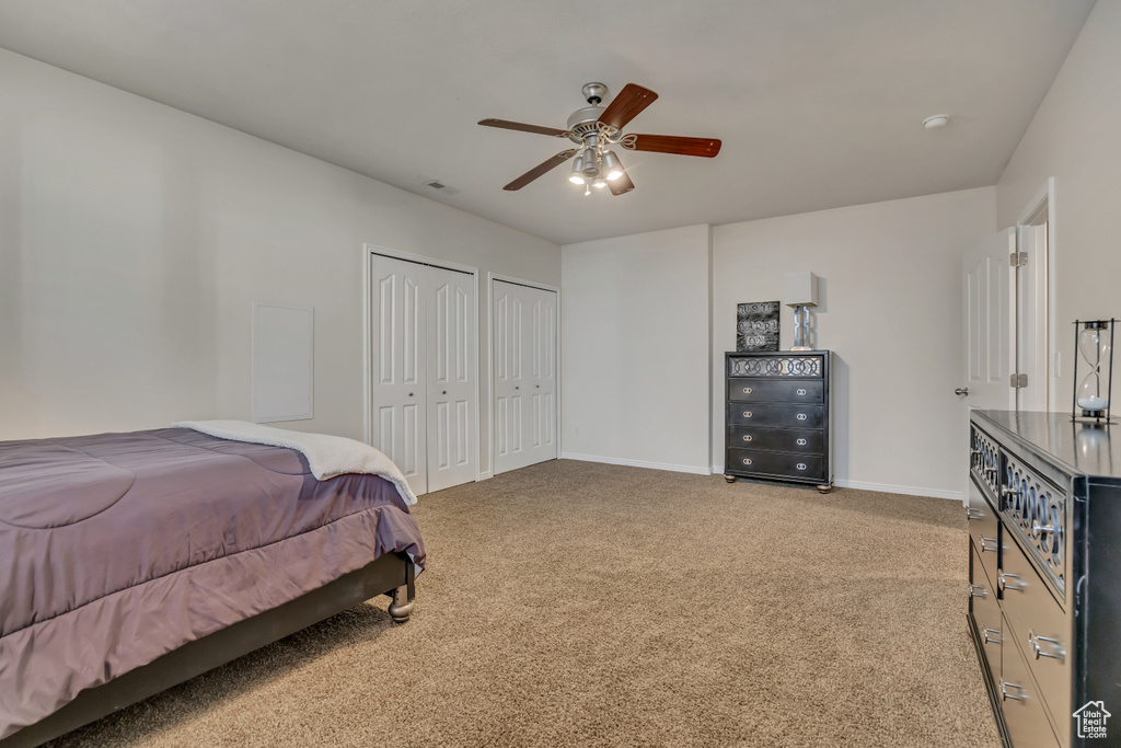 Bedroom with two closets, light colored carpet, baseboards, and a ceiling fan