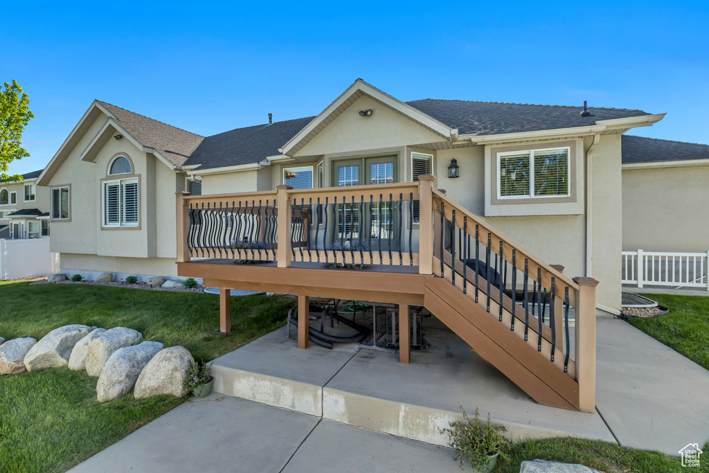 Rear view of property featuring stucco siding, a lawn, and a deck