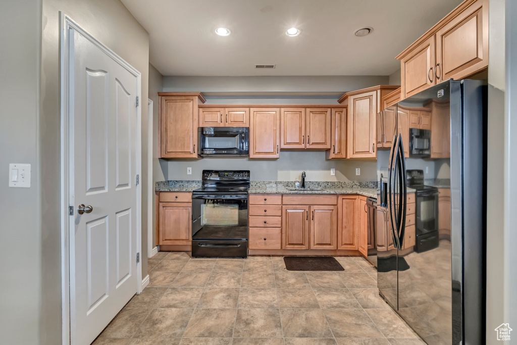 Kitchen featuring black appliances, recessed lighting, light stone countertops, and a sink