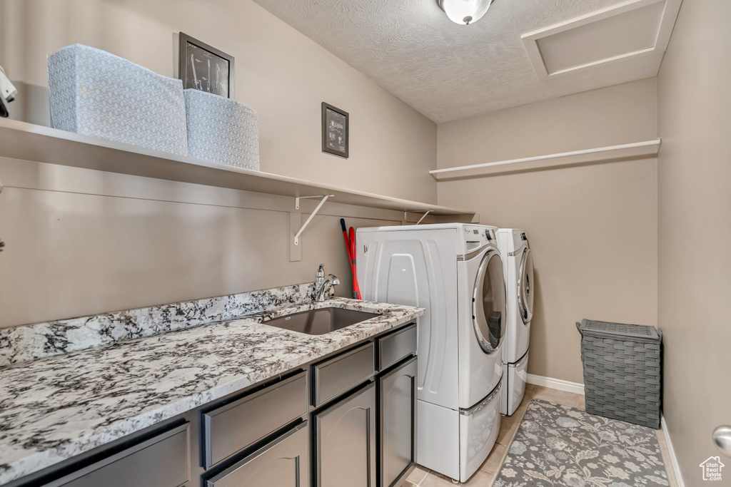 Laundry area featuring separate washer and dryer, cabinet space, light tile patterned floors, baseboards, and a textured ceiling