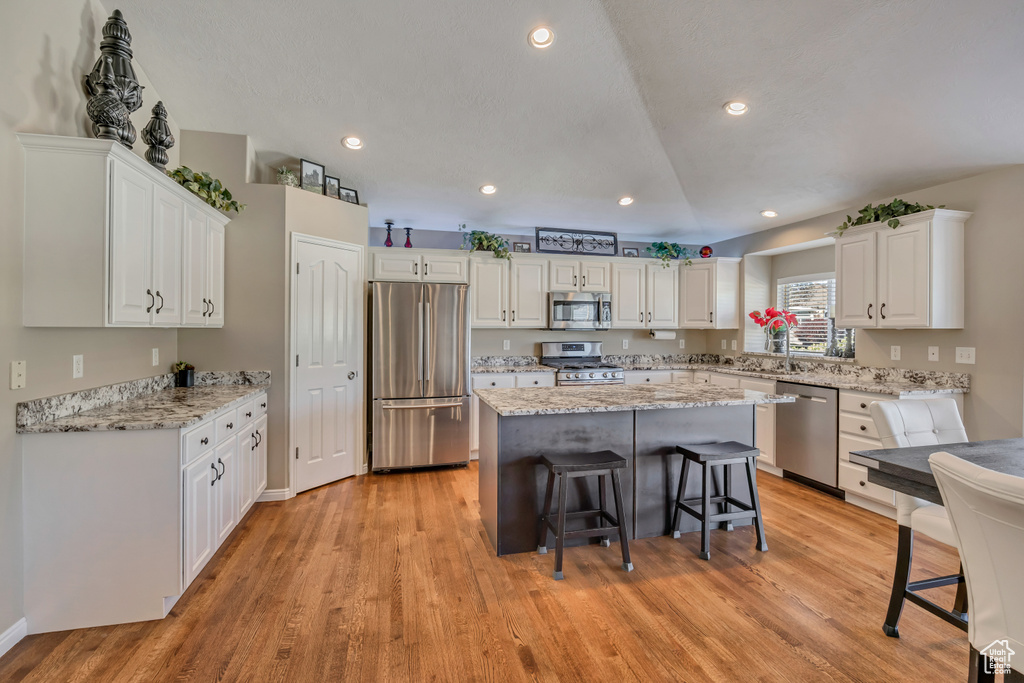 Kitchen with stainless steel appliances, white cabinets, a kitchen bar, a center island, and light wood-type flooring