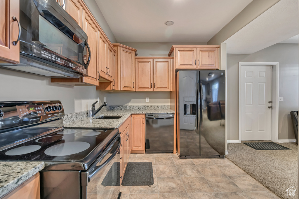 Kitchen featuring black appliances, a sink, light stone counters, light brown cabinetry, and light colored carpet