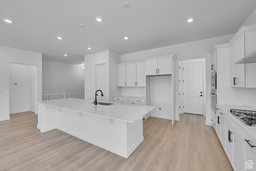 Kitchen featuring a sink, appliances with stainless steel finishes, light wood-style flooring, a kitchen island with sink, and recessed lighting