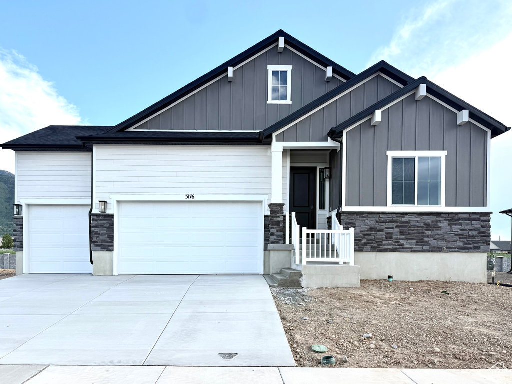 View of front of house featuring board and batten siding, stone siding, driveway, and a garage