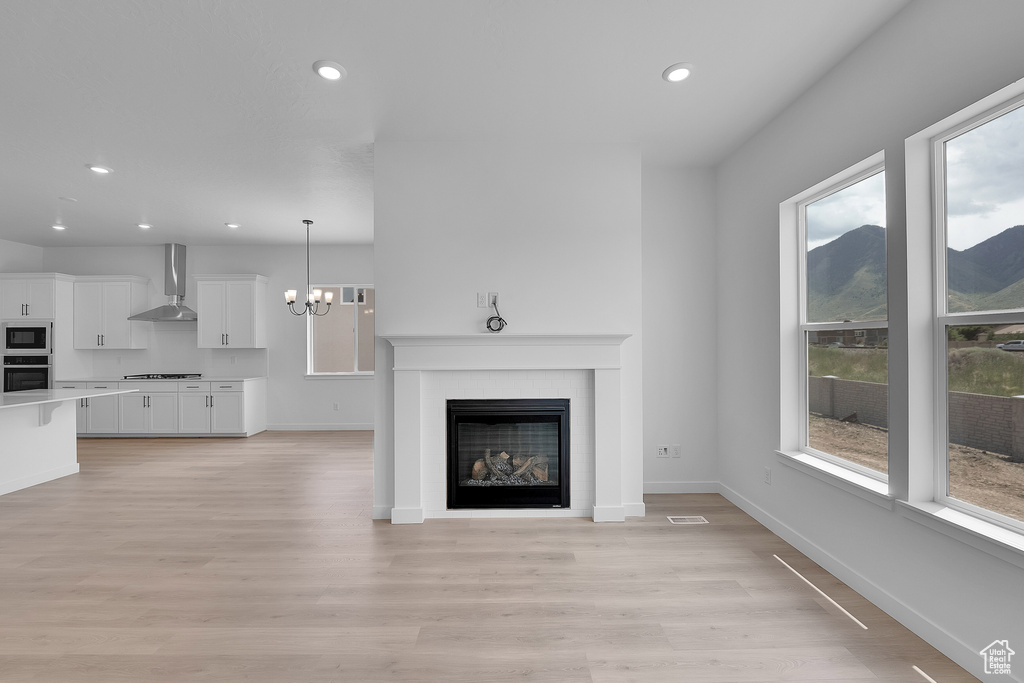 Unfurnished living room featuring plenty of natural light, recessed lighting, light wood-style flooring, baseboards, and a chandelier