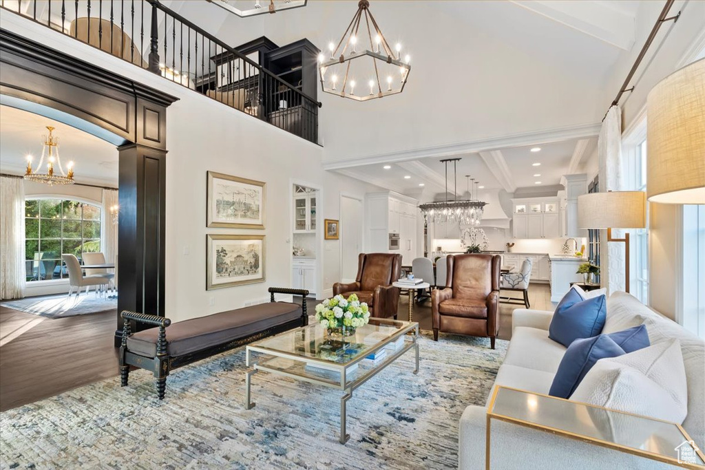Living area with a chandelier, wood finished floors, a towering ceiling, beamed ceiling, and ornamental molding