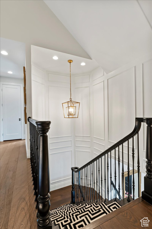 Stairway featuring a decorative wall, wood finished floors, recessed lighting, a chandelier, and lofted ceiling