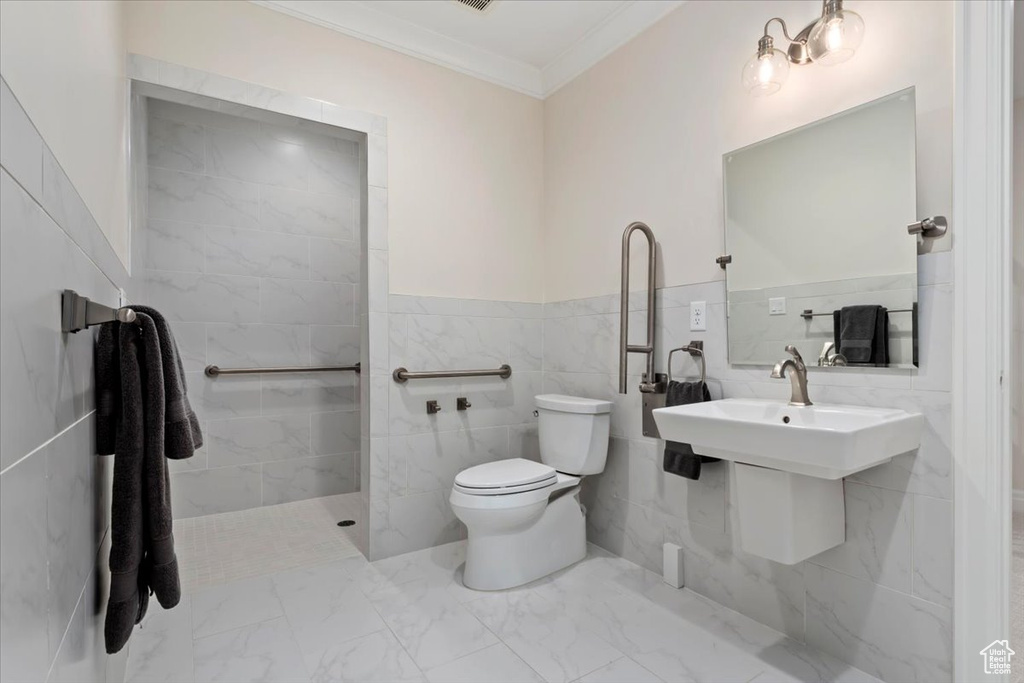 Bathroom featuring crown molding, toilet, tile walls, marble look tiles, and a wainscoted wall