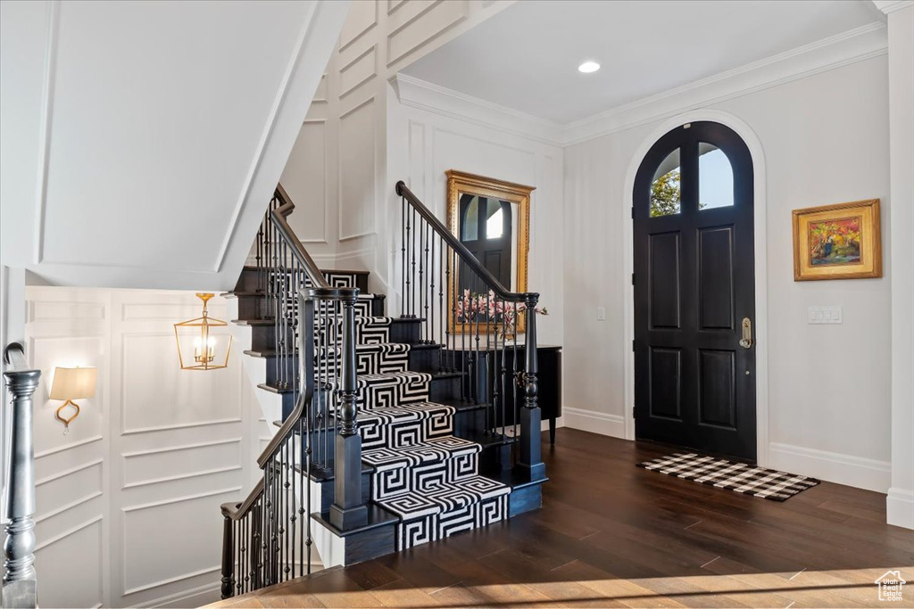 Foyer with baseboards, wood finished floors, arched walkways, ornamental molding, and a decorative wall