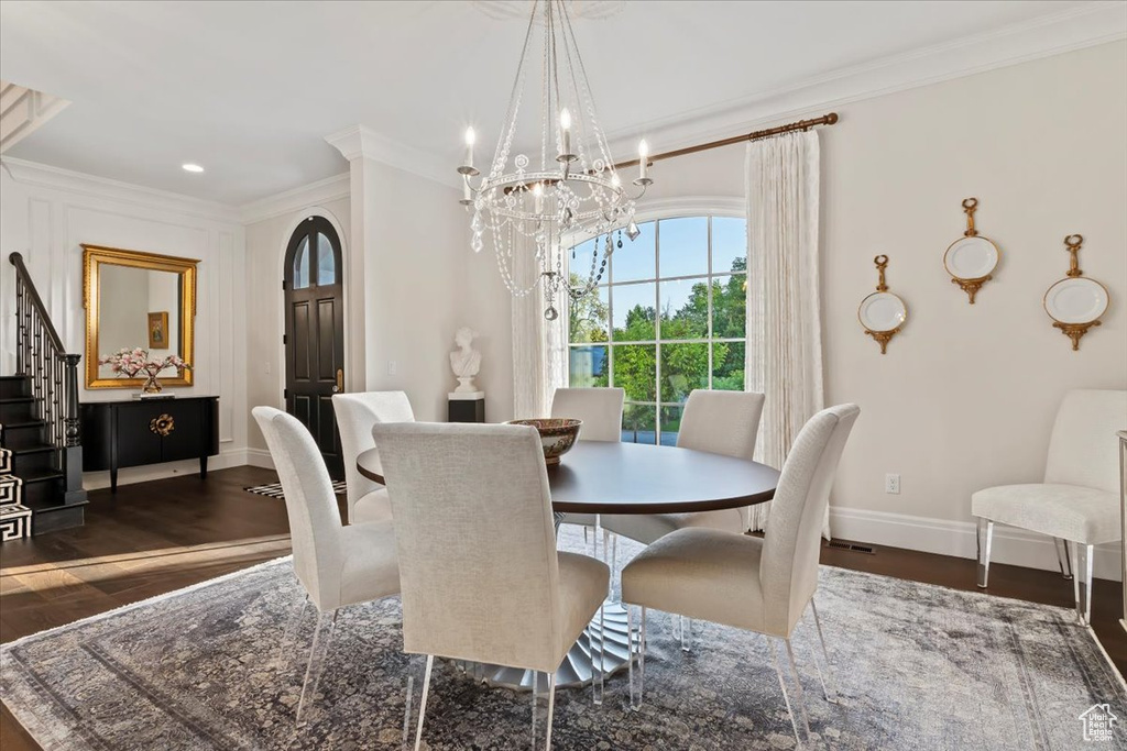 Dining area featuring a chandelier, ornamental molding, wood finished floors, baseboards, and stairway