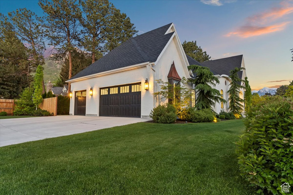 Property exterior at dusk featuring a garage, driveway, roof with shingles, and stucco siding