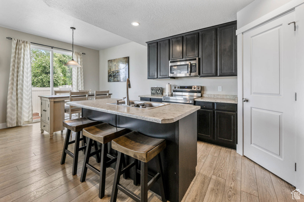 Kitchen featuring stainless steel appliances, a sink, light wood finished floors, light countertops, and a kitchen breakfast bar