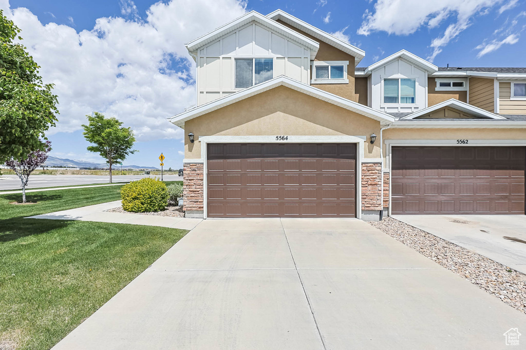 View of front of house with stone siding, concrete driveway, a front yard, and stucco siding