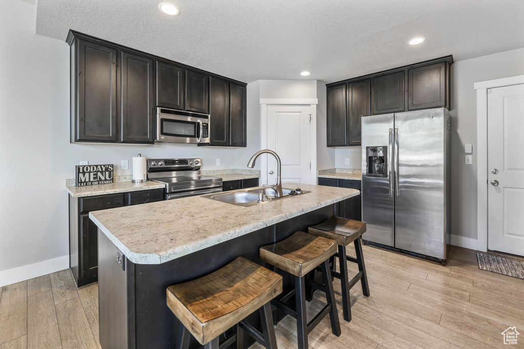 Kitchen featuring stainless steel appliances, a sink, light wood finished floors, baseboards, and a kitchen breakfast bar