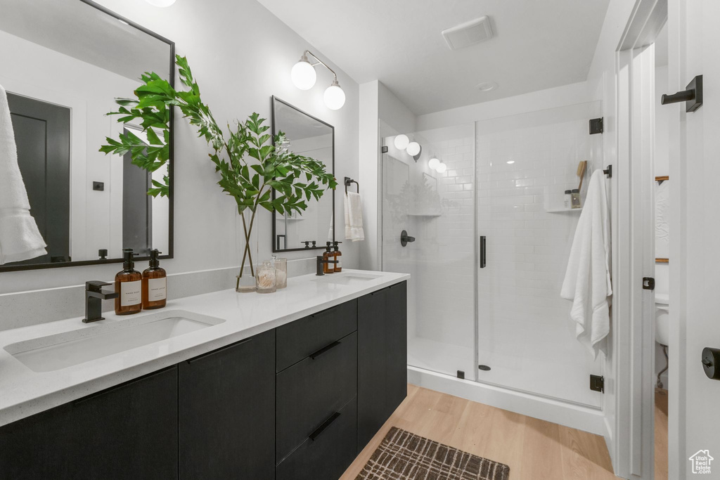 Full bath with double vanity, a stall shower, wood finished floors, and toilet