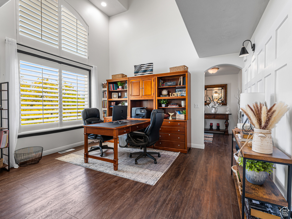 Office area featuring a high ceiling, baseboards, dark wood-style floors, arched walkways, and recessed lighting